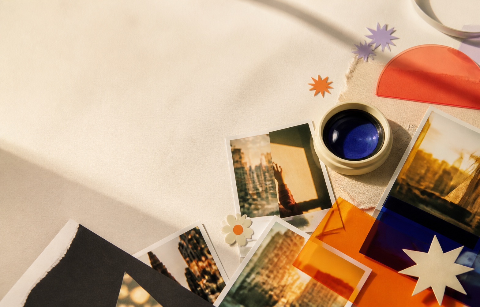 A sunlit creative table with photographs, colorful paper and a camera lens